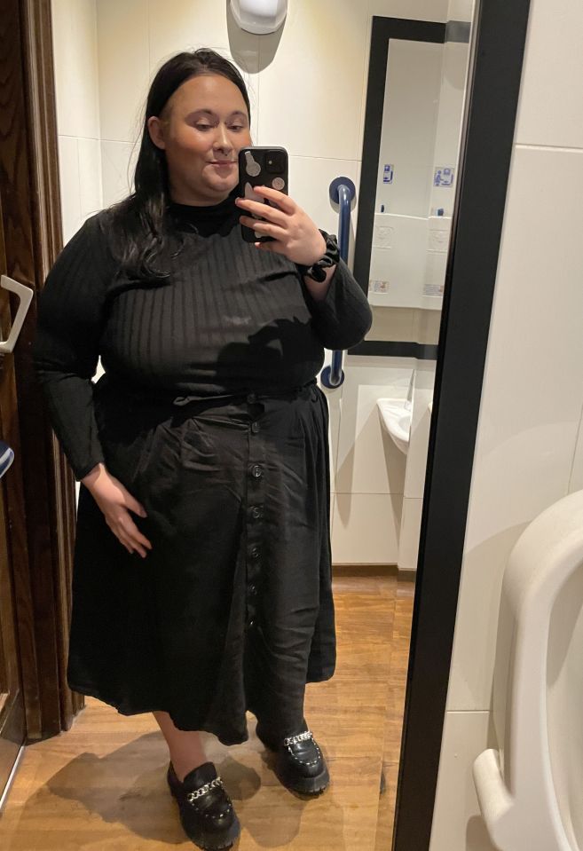 Woman in black outfit taking a selfie in a restroom.