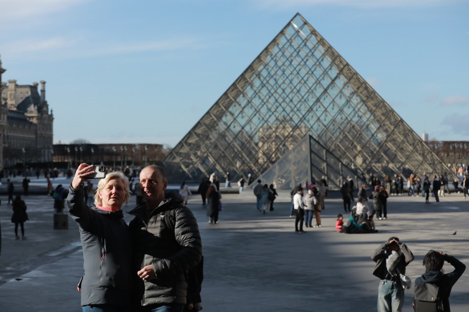 Couple taking a selfie in front of the Louvre Pyramid in Paris.