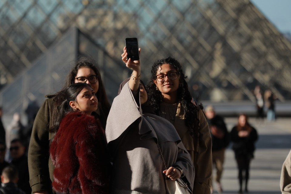 Person photographing the Mona Lisa at the Louvre Museum.