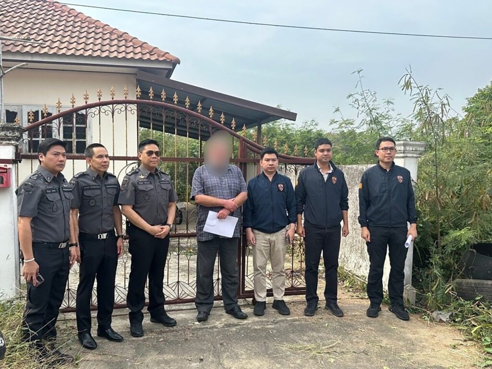 Police officers and a suspect stand outside a house.