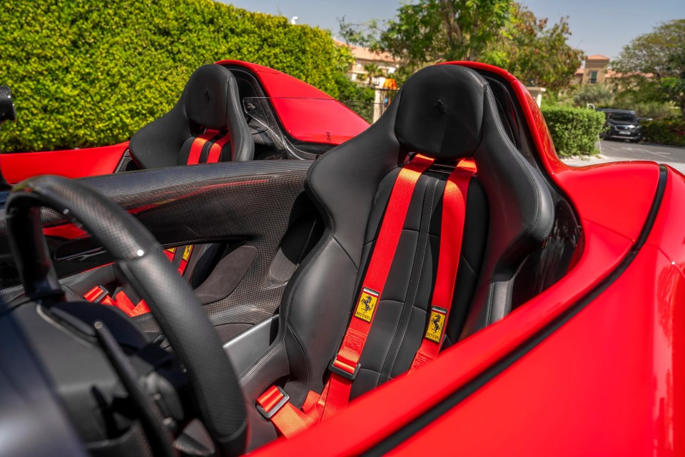 Close-up of a red Ferrari Monza SP2's interior, showing carbon fiber details and red seatbelts.