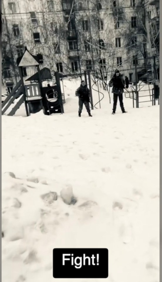 Two people standing in the snow near a playground.