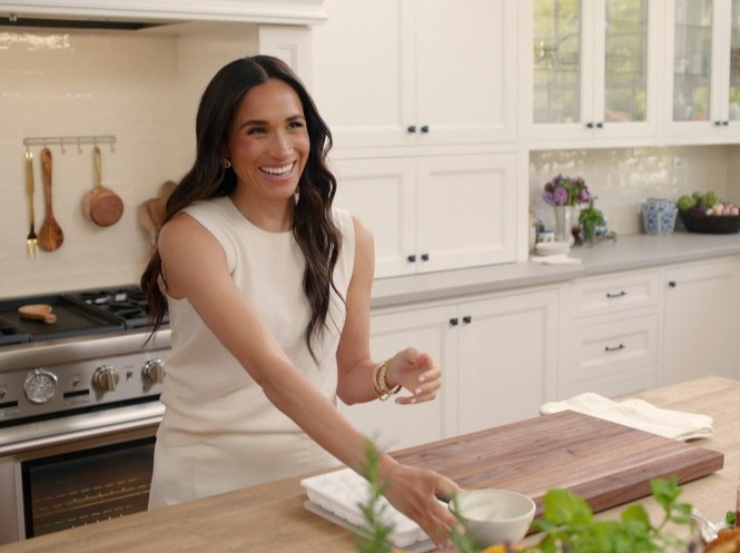 A woman smiling in a kitchen preparing food.