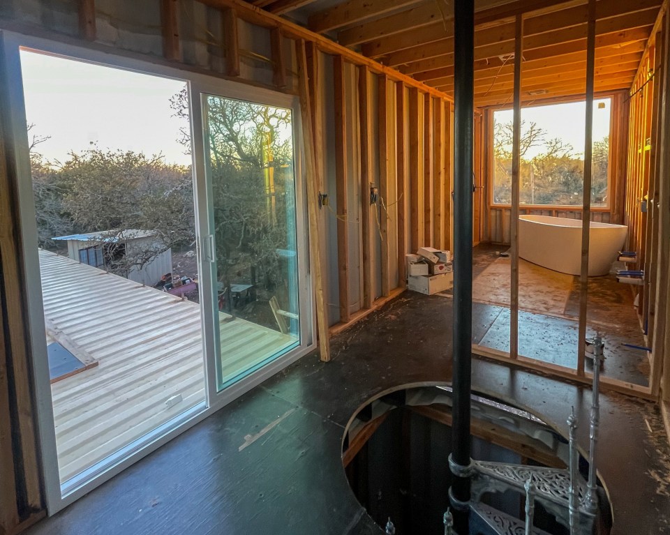 Interior view of a shipping container home under construction, showing a bathtub and staircase.