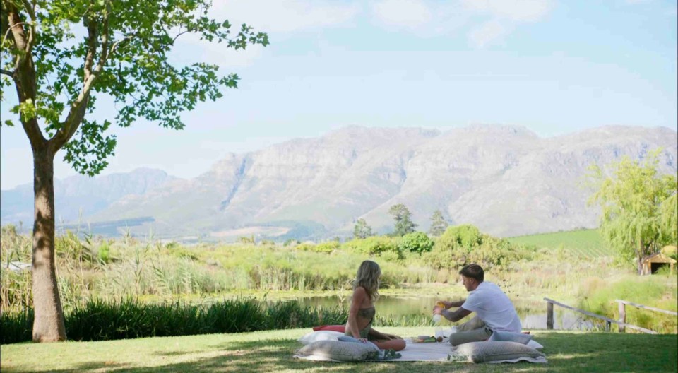 Couple on a picnic by a pond with mountains in the background.