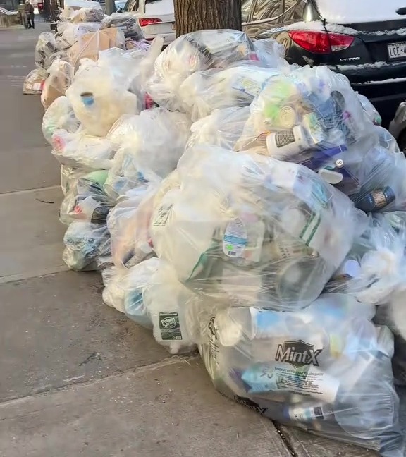 Pile of garbage bags on a city sidewalk.