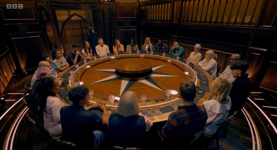 A group of people sitting around a large, circular table in a dimly lit room.