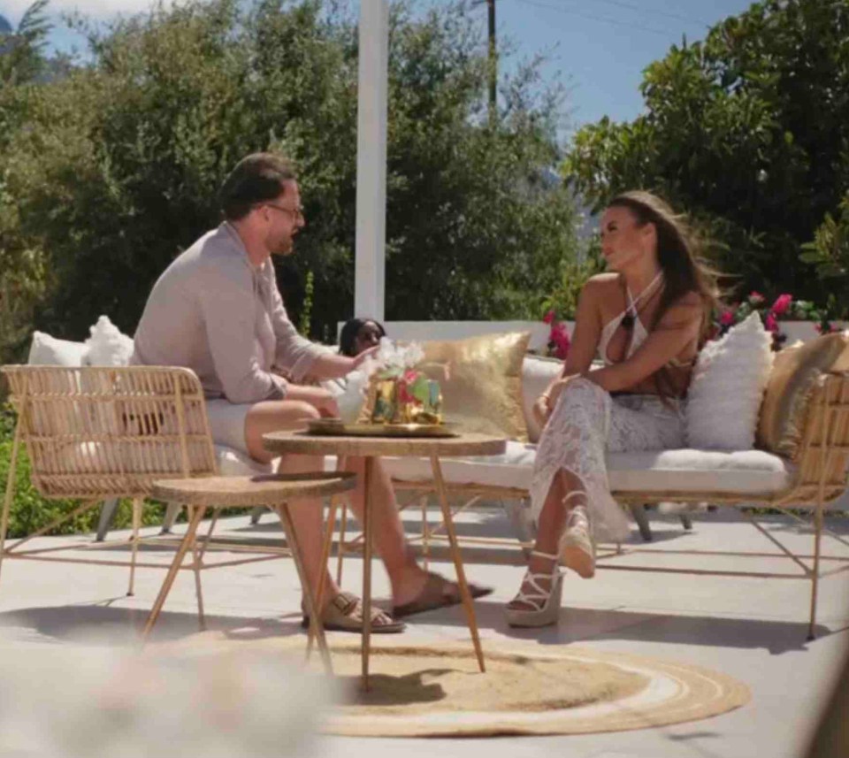 Couple sitting outdoors on patio furniture, talking.