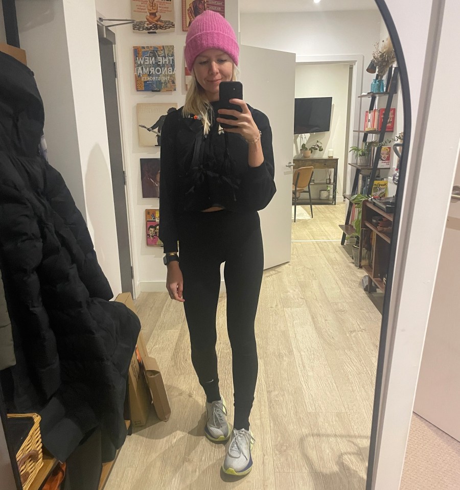 Woman in pink beanie and black workout clothes taking a selfie in a mirror.