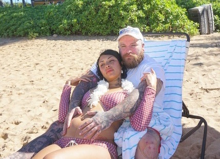 Pregnant woman and man embracing on a beach.