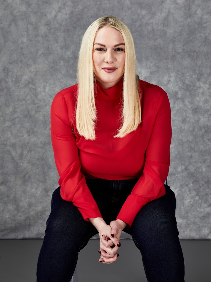 Portrait of Elizabeth G. in a red shirt and dark jeans.