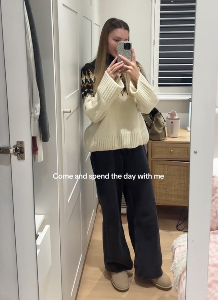 Zara McDermott in a cream sweater and black pants, taking a selfie in a mirror.