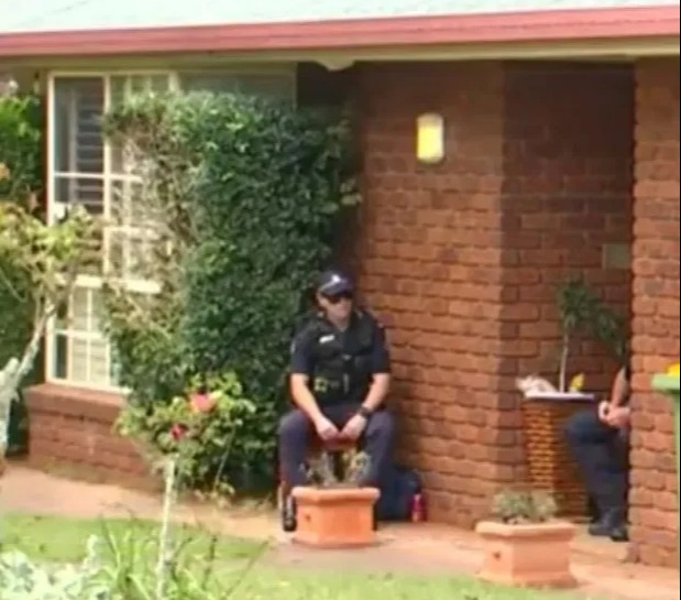 Two police officers sitting outside a brick house.