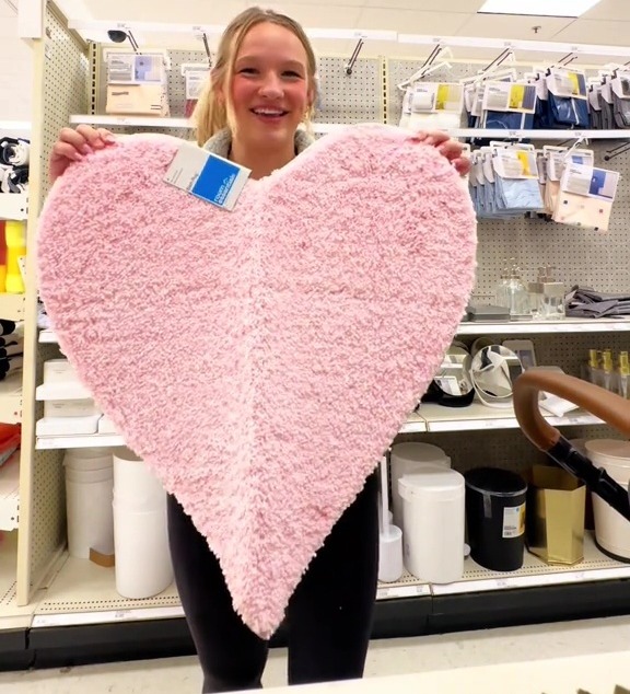 Woman holding a pink heart-shaped rug in a store.