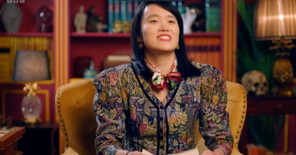 Woman in patterned blouse sits in armchair, reading.