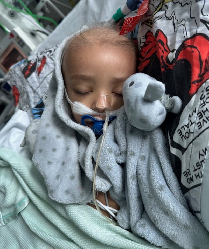 Young boy sleeping in a hospital bed, connected to medical equipment.