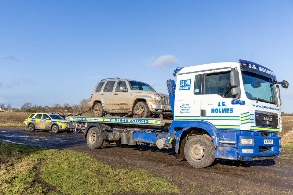 A muddy SUV being towed away by a recovery truck, with police present.