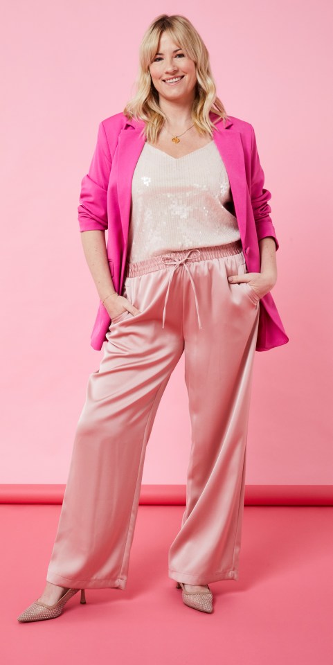 Woman in pink blazer and satin pants against a pink background.