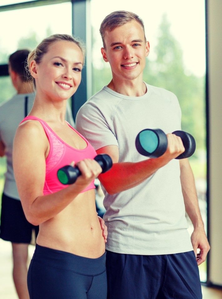 Young woman and her personal trainer lifting weights at the gym.