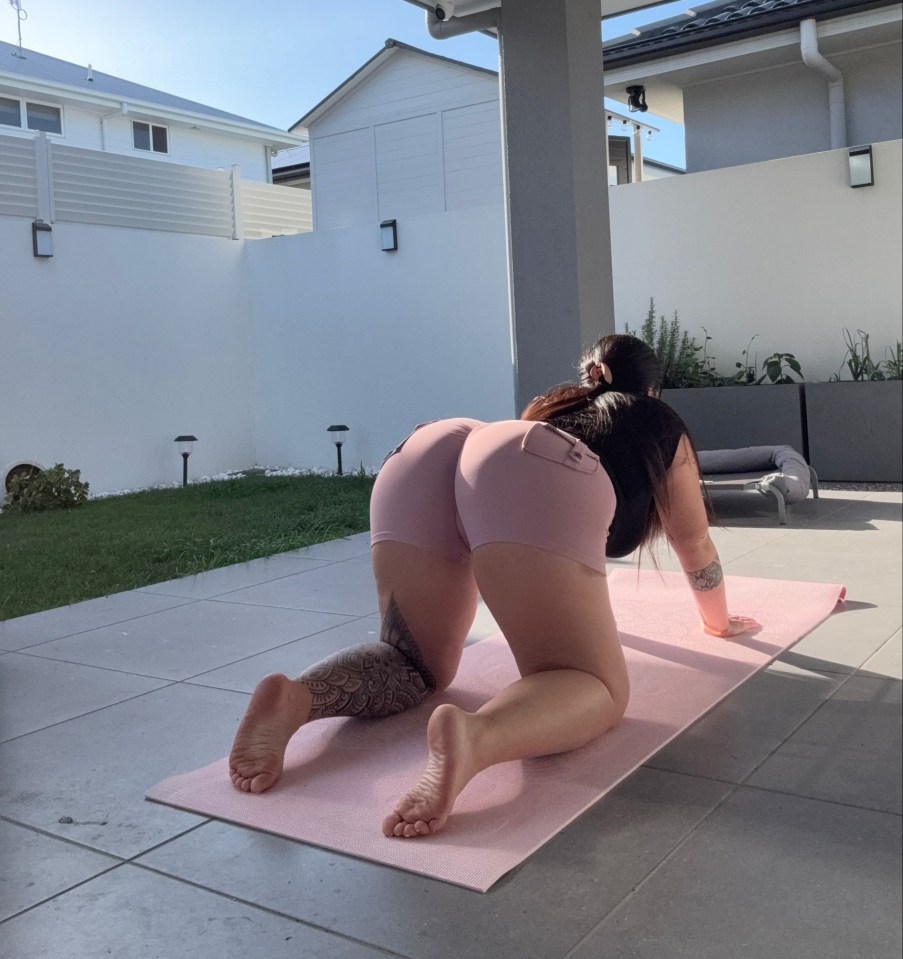 Woman doing yoga on a pink mat outside.