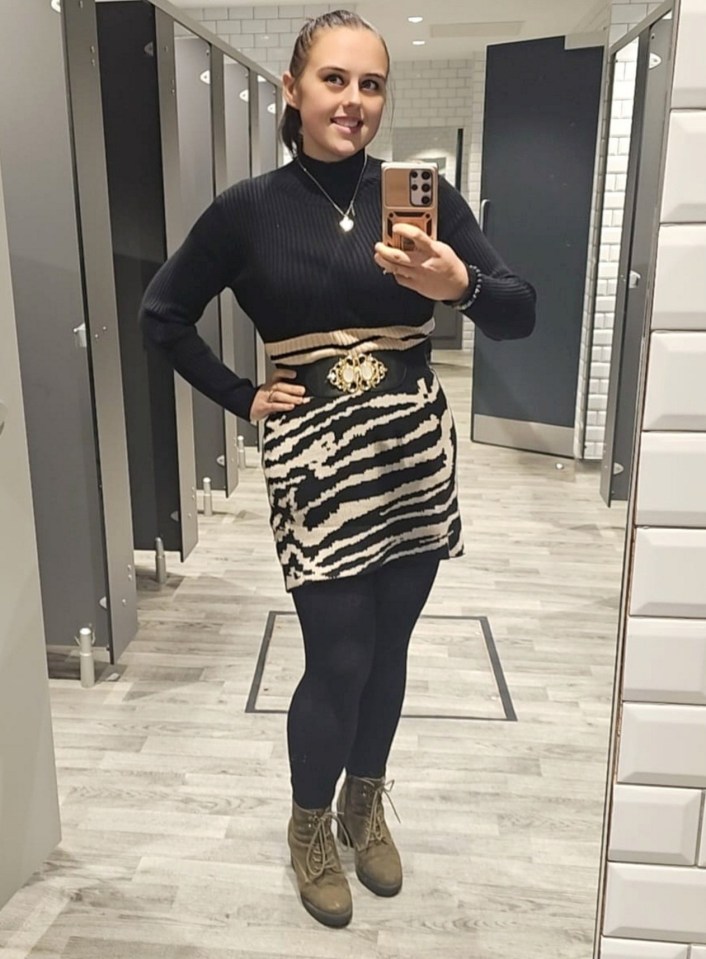 Woman taking a selfie in a restroom mirror wearing a zebra-striped dress and boots.