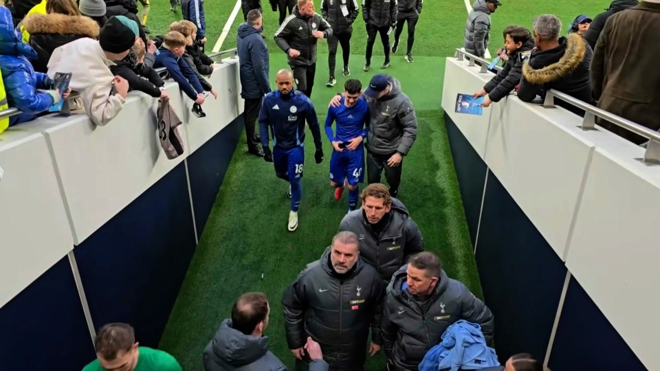 Soccer players leaving the field, escorted by staff.