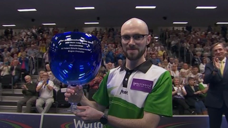 A man holding a blue trophy in front of a cheering audience.