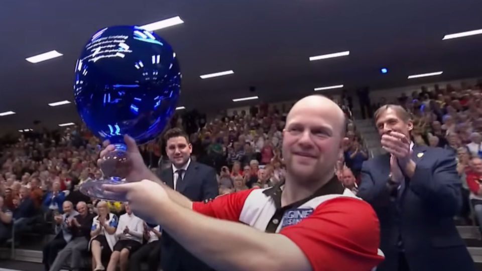 A man holding a large blue trophy in front of a cheering audience.