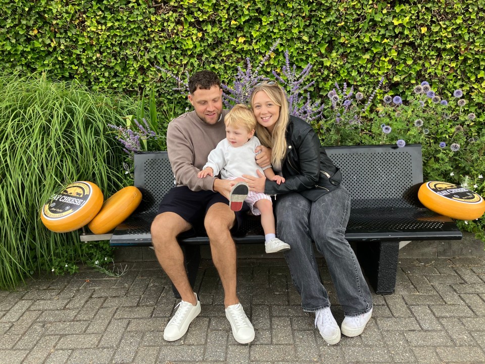 Family sitting on a bench with cheese wheels.