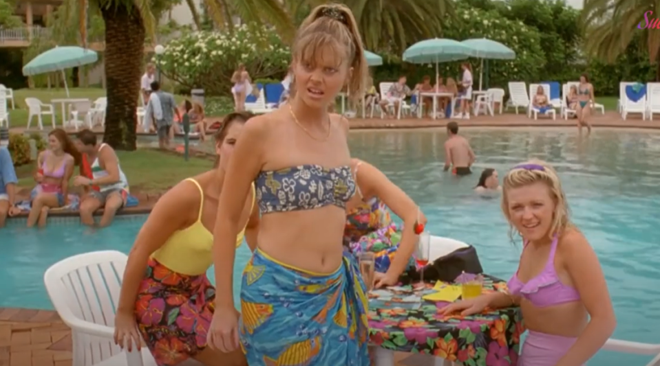 Three young women in swimsuits by a pool.