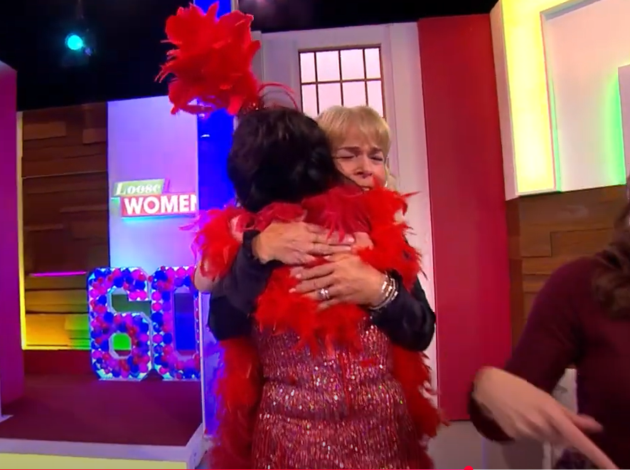 Two women hugging on a television show set.