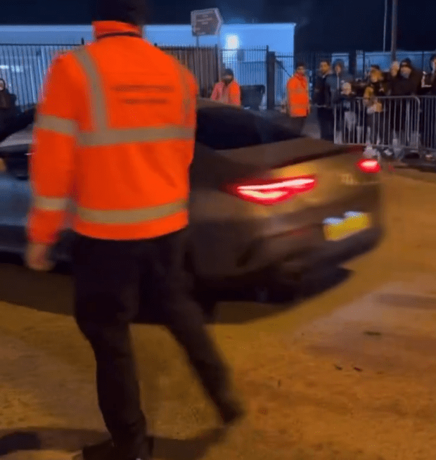 Security guard guiding a car past a crowd.