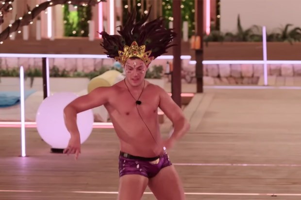 Man in headdress and swim trunks dancing.