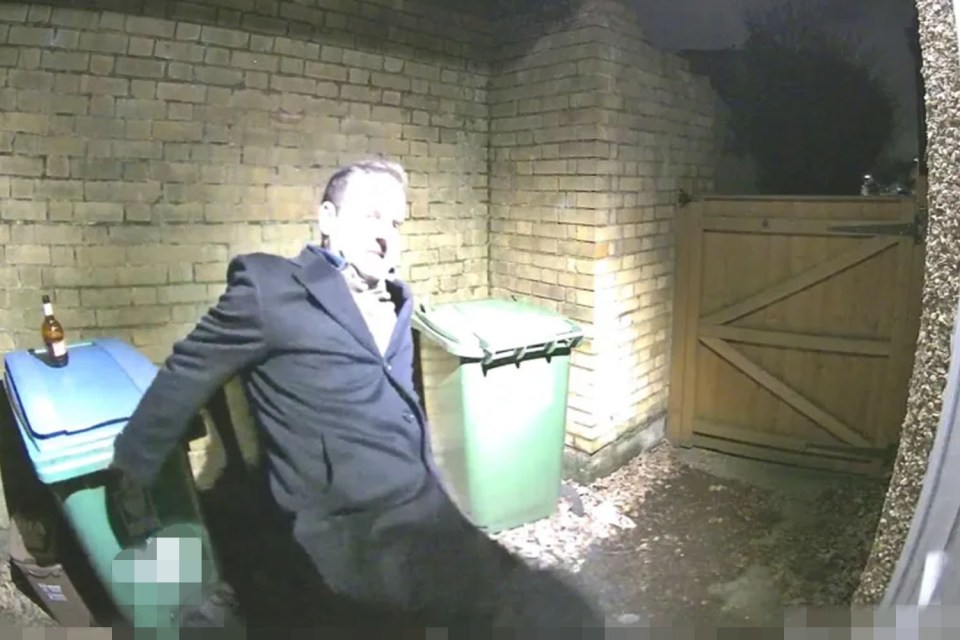 Man leaning against a bin, holding a bottle.