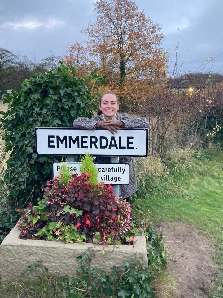 Woman smiling at Emmerdale village sign.