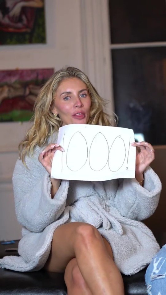 Woman in bathrobe holding a sign that says "1000!"