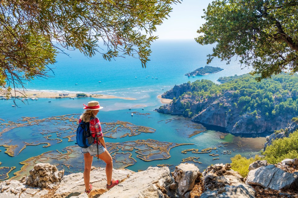 Woman overlooking a beach and turquoise water from a rocky outcrop.