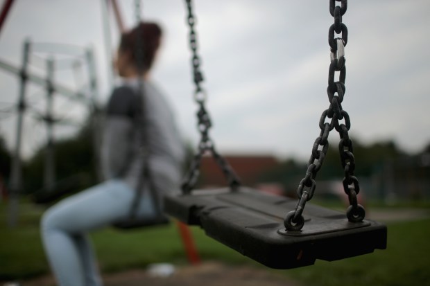 A blurry figure sits on a swing set, in the foreground is the swing set in focus.