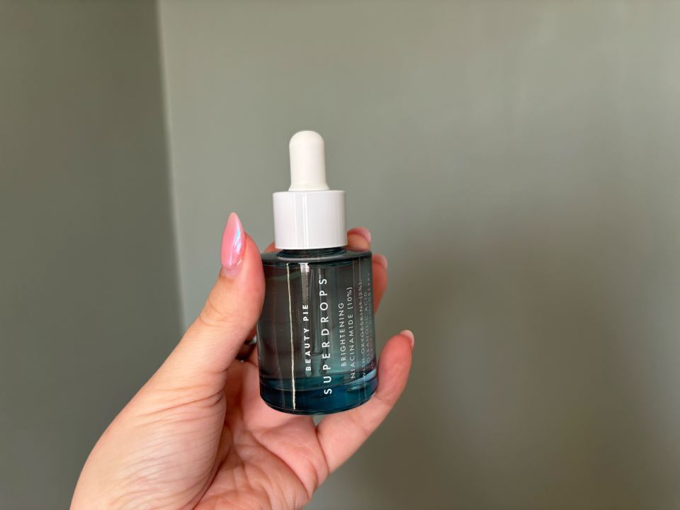 Hand holding Beauty Pie Superdrops brightening serum bottle.