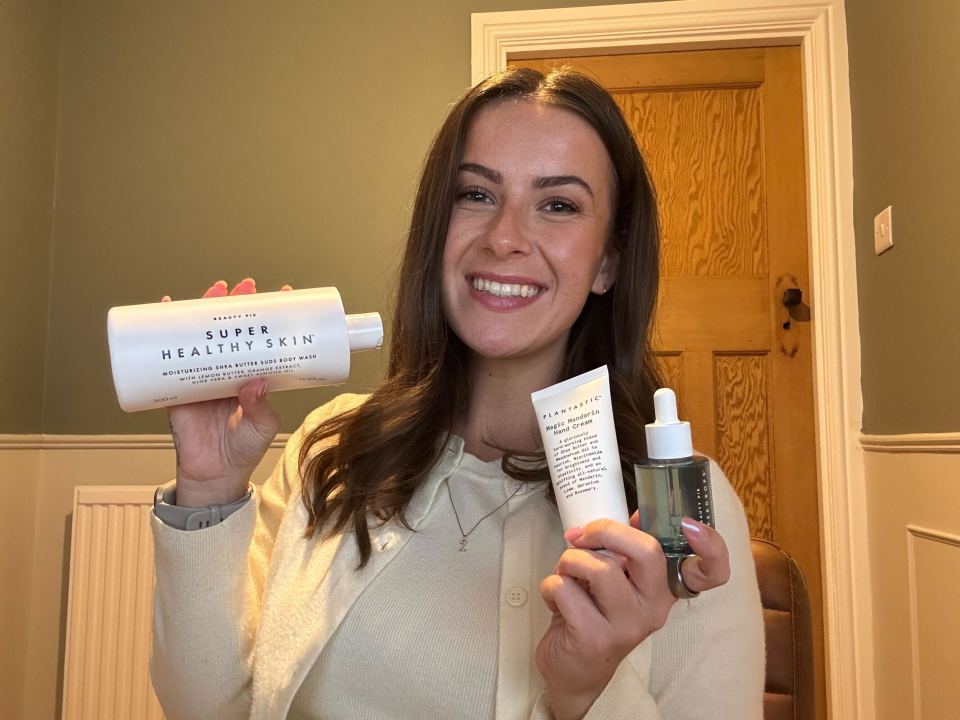 Woman holding body wash, hand cream, and face oil.