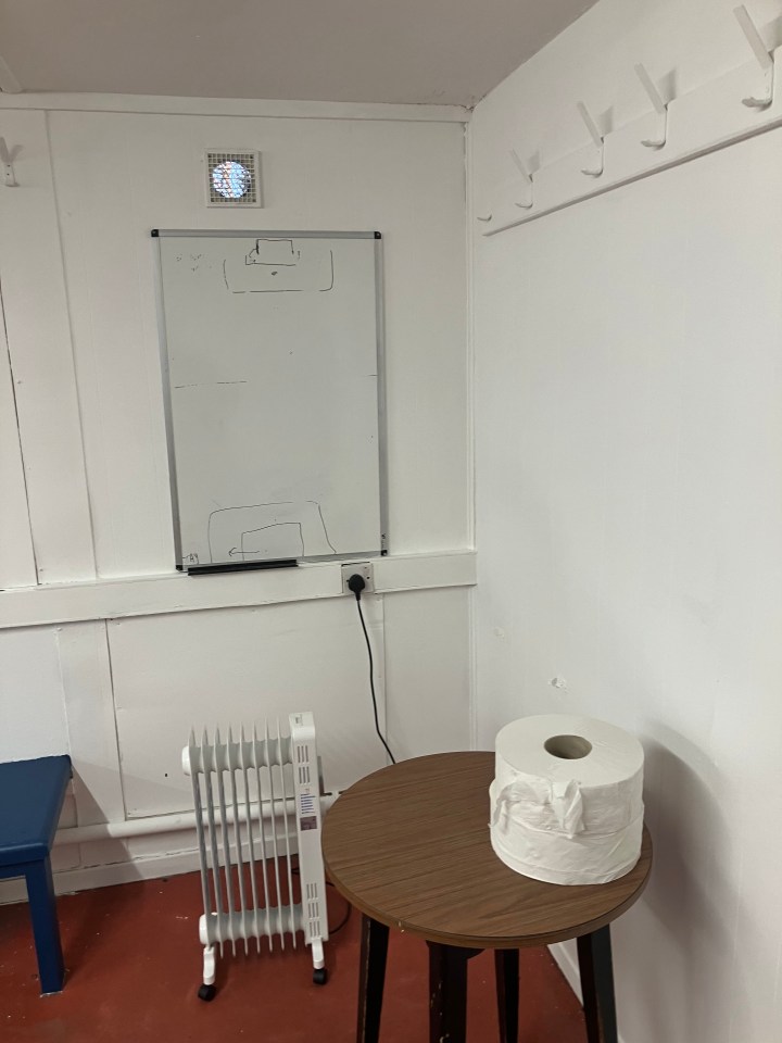 A whiteboard with a tactical diagram, a heater, and a roll of toilet paper on a small table in a room.