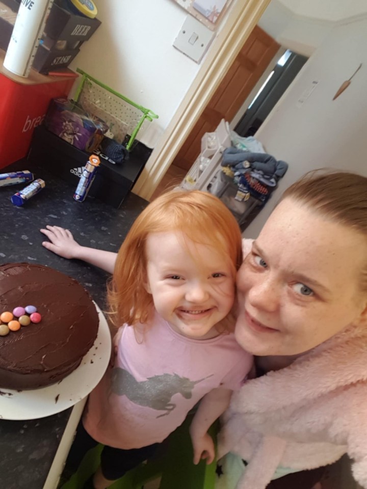 A woman and young girl smile next to a chocolate cake.