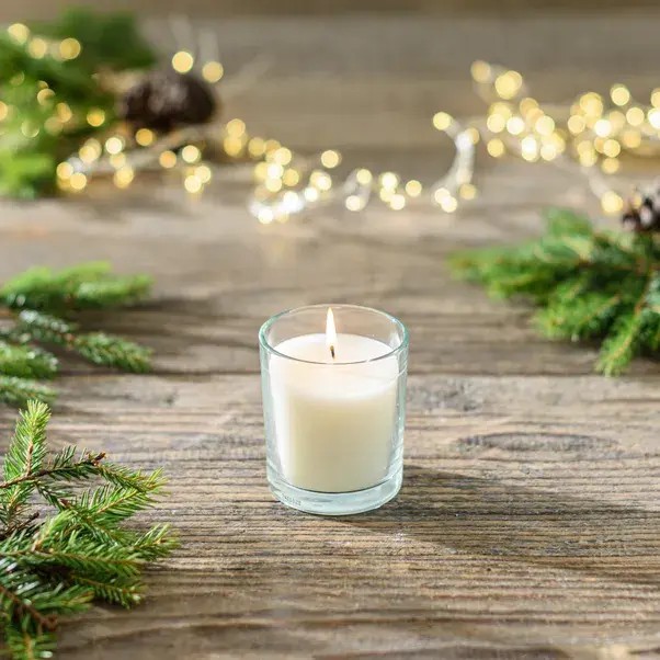 Lit candle on a wooden surface with evergreen branches and fairy lights.