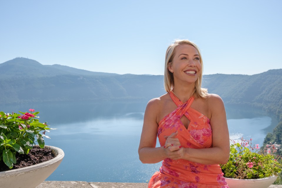 Woman in orange dress smiles while overlooking a lake and mountains.