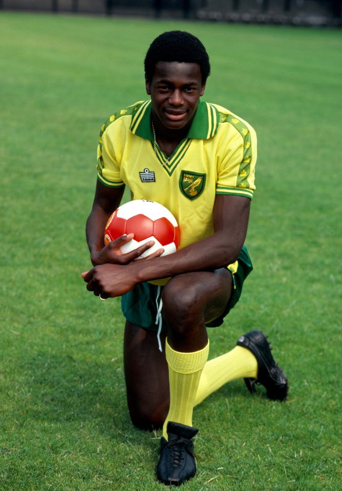 Justin Fashanu kneeling on a field, holding a soccer ball.