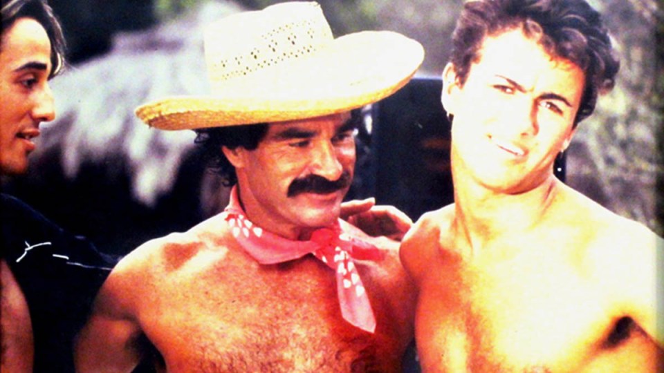 Three shirtless men; one wears a straw cowboy hat and red bandana.