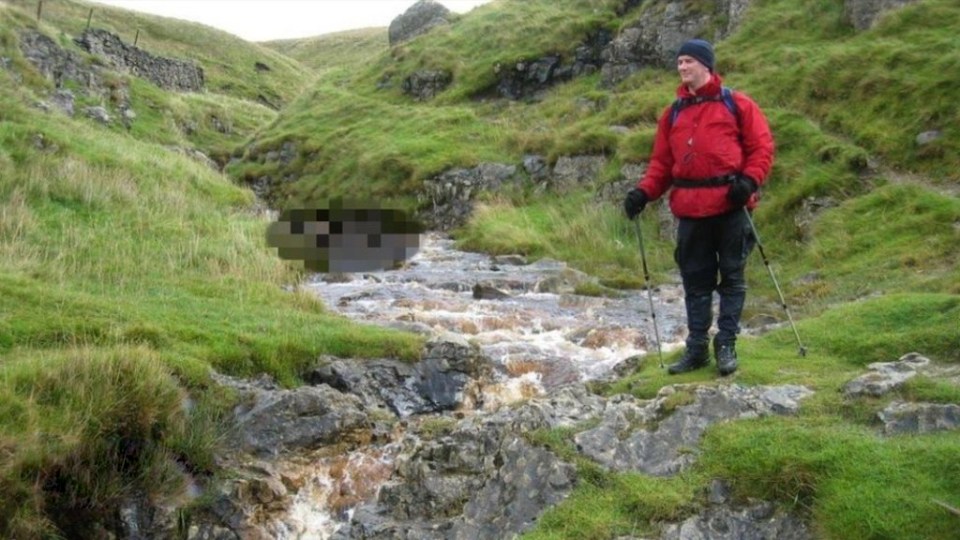 Hiker with trekking poles crossing a stream in a mountainous area.