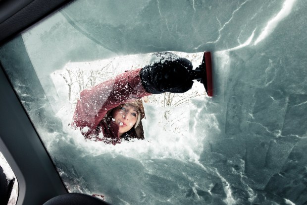 Woman clearing snow from car windshield.