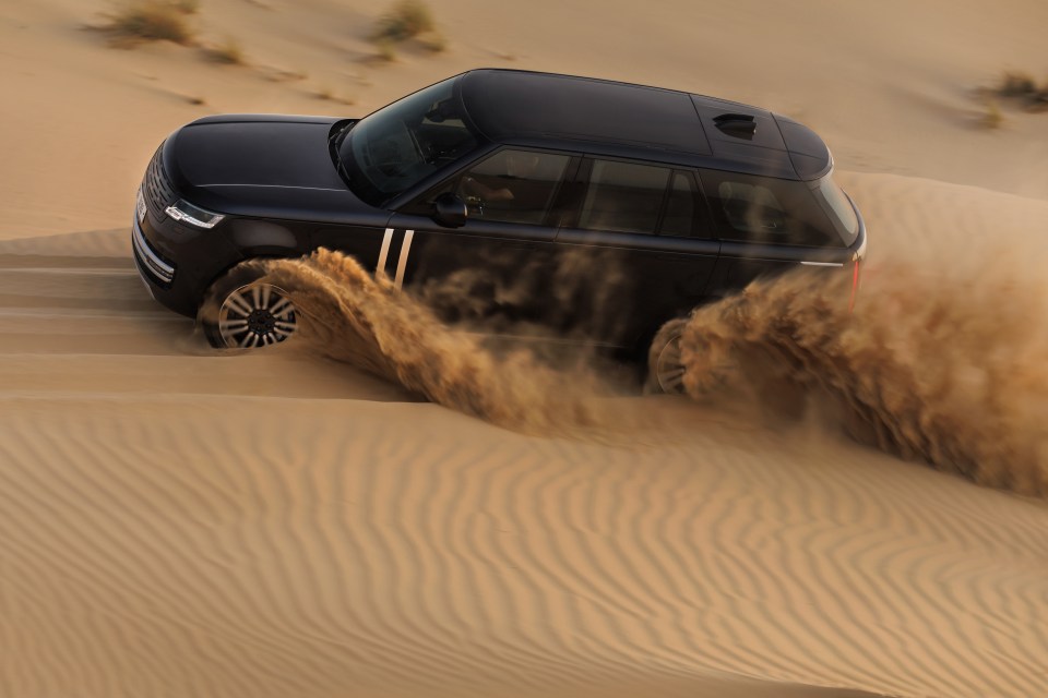 Black SUV driving through sand dunes.