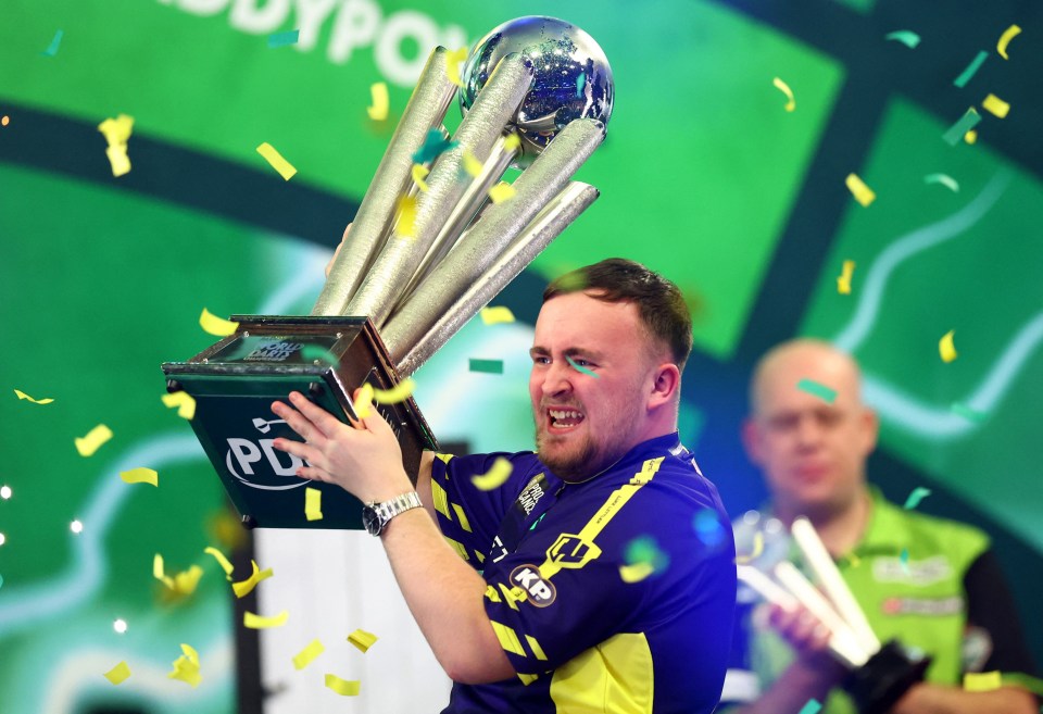 Luke Littler holding the PDC World Darts Championship trophy.